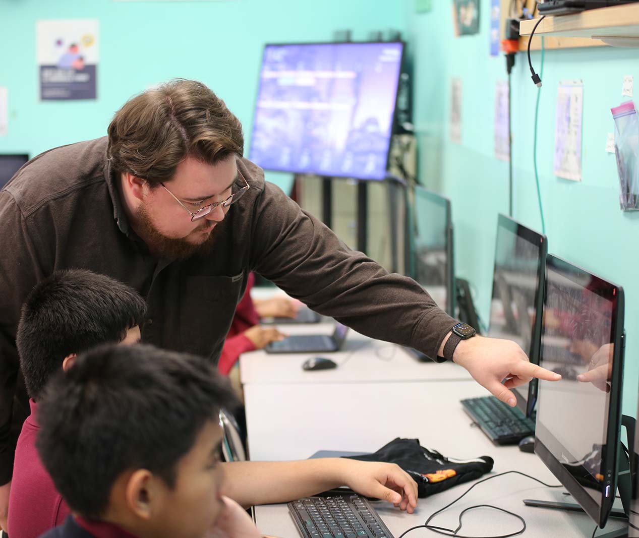 HSA Teacher smiles while kneeling beside a young student in a classroom setting.